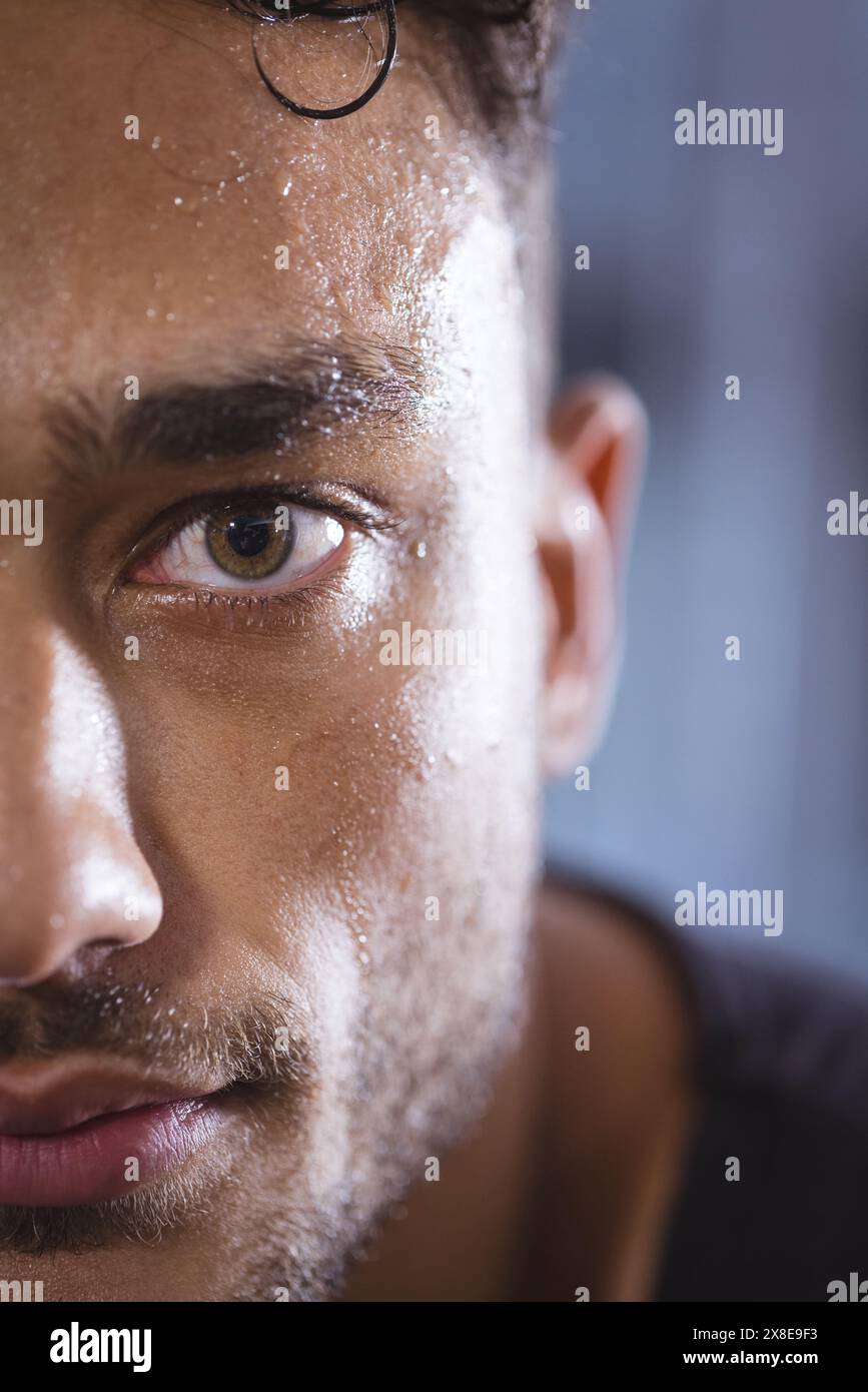 At gym, biracial man with fit physique sweating after intense workout. Gym equipment and weights visible in blurred background, indicating fitness env Stock Photo