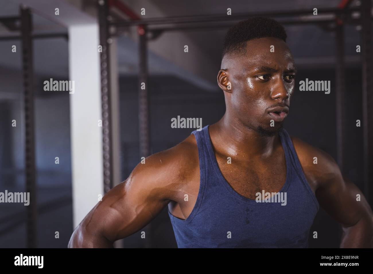 Strong and fit African American man in his mid-twenties working out at gym. He is standing in front of gym equipment, sweating and focused on his exer Stock Photo