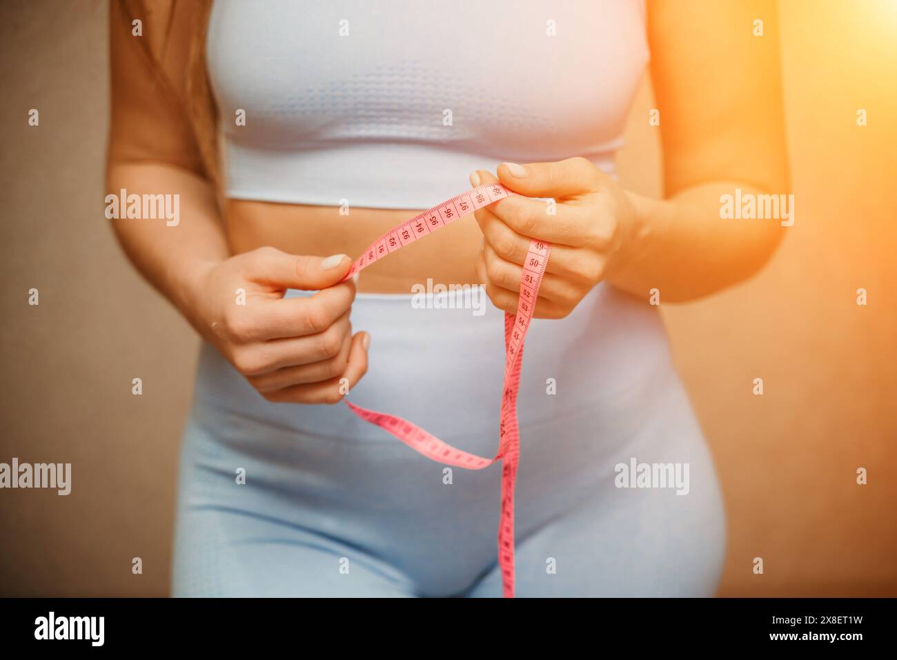 Cropped view of slim woman measuring waist with tape measure at home, close up. European woman checking the result of diet for weight loss or Stock Photo