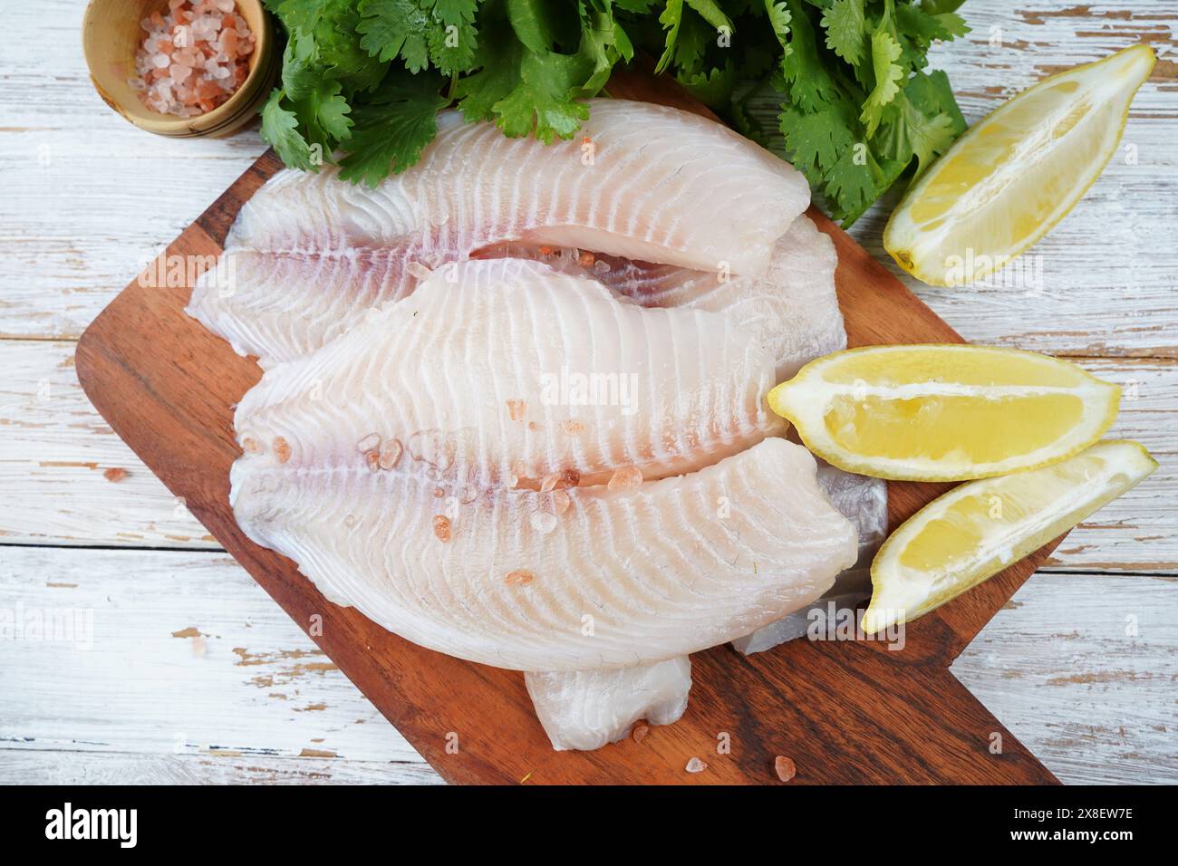 Fresh tilapia fish fillet sliced for steak or salad with herbs spices and lemon Stock Photo