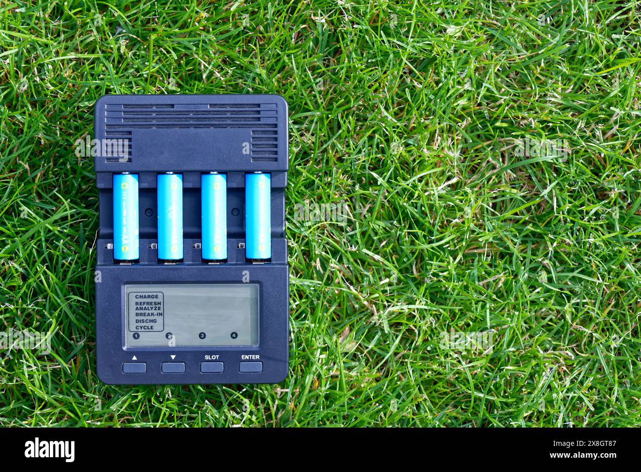 AA battery charger with rechargeable AA type batteries on green grass Stock Photo