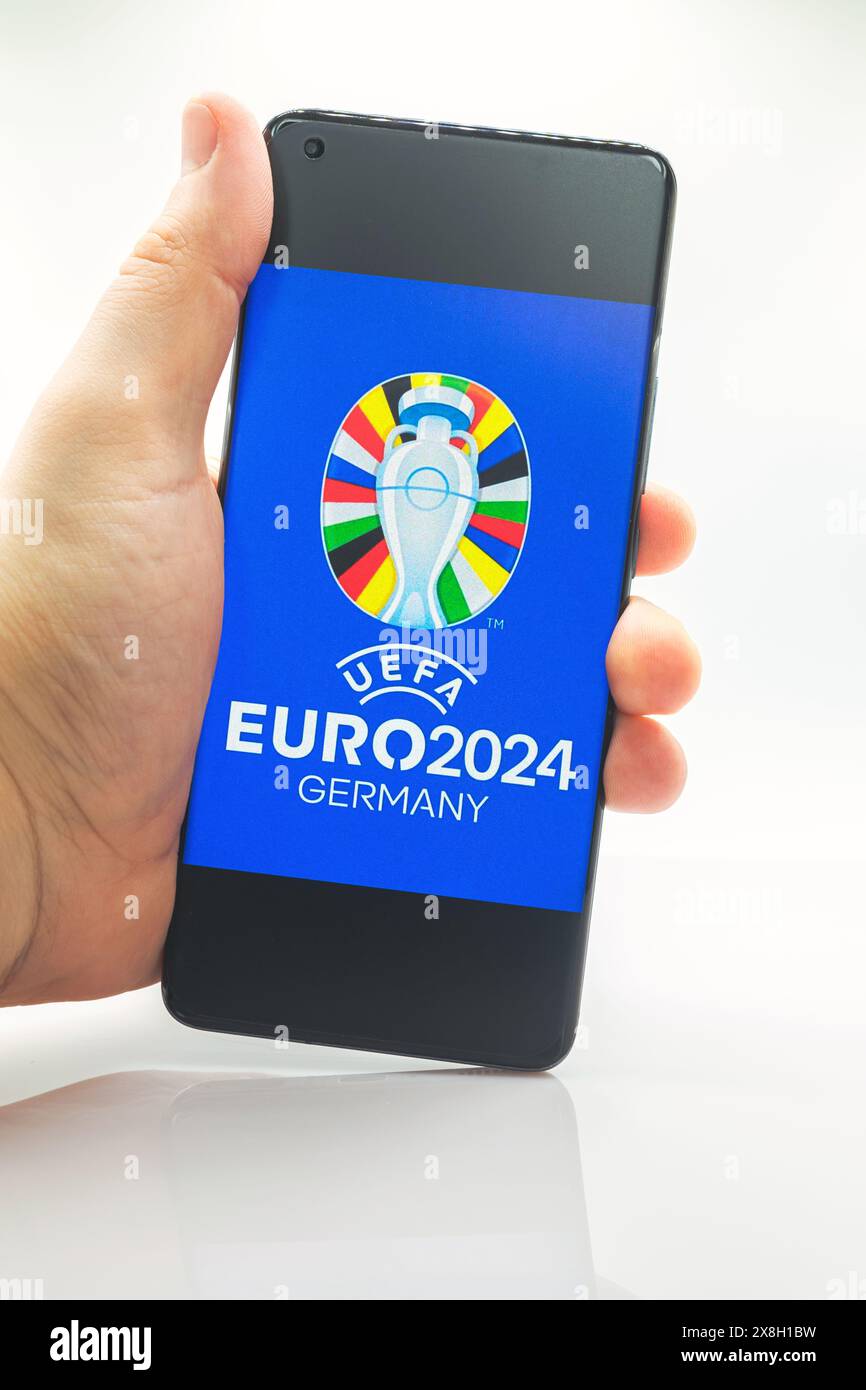 A man is holding a smartphone with the official logo of the UEFA European Football Championship 2024 on the mobile phone screen Stock Photo