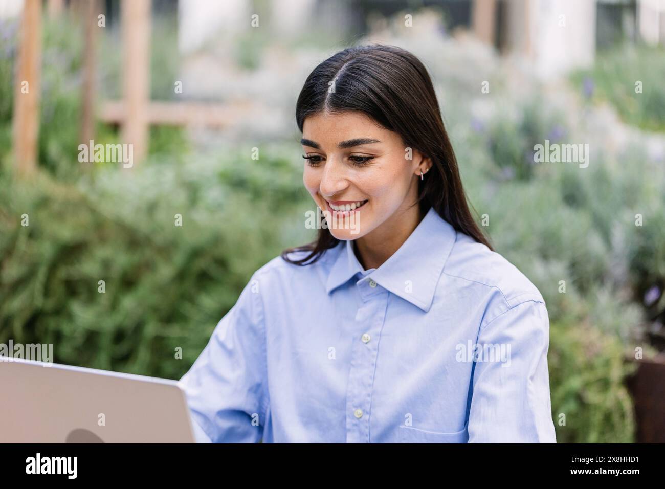 Happy young woman working remotely on laptop sitting outside Stock Photo
