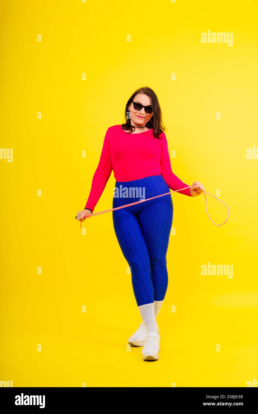 Pretty smiling plump female in sporty top and leggings holding jumping ...