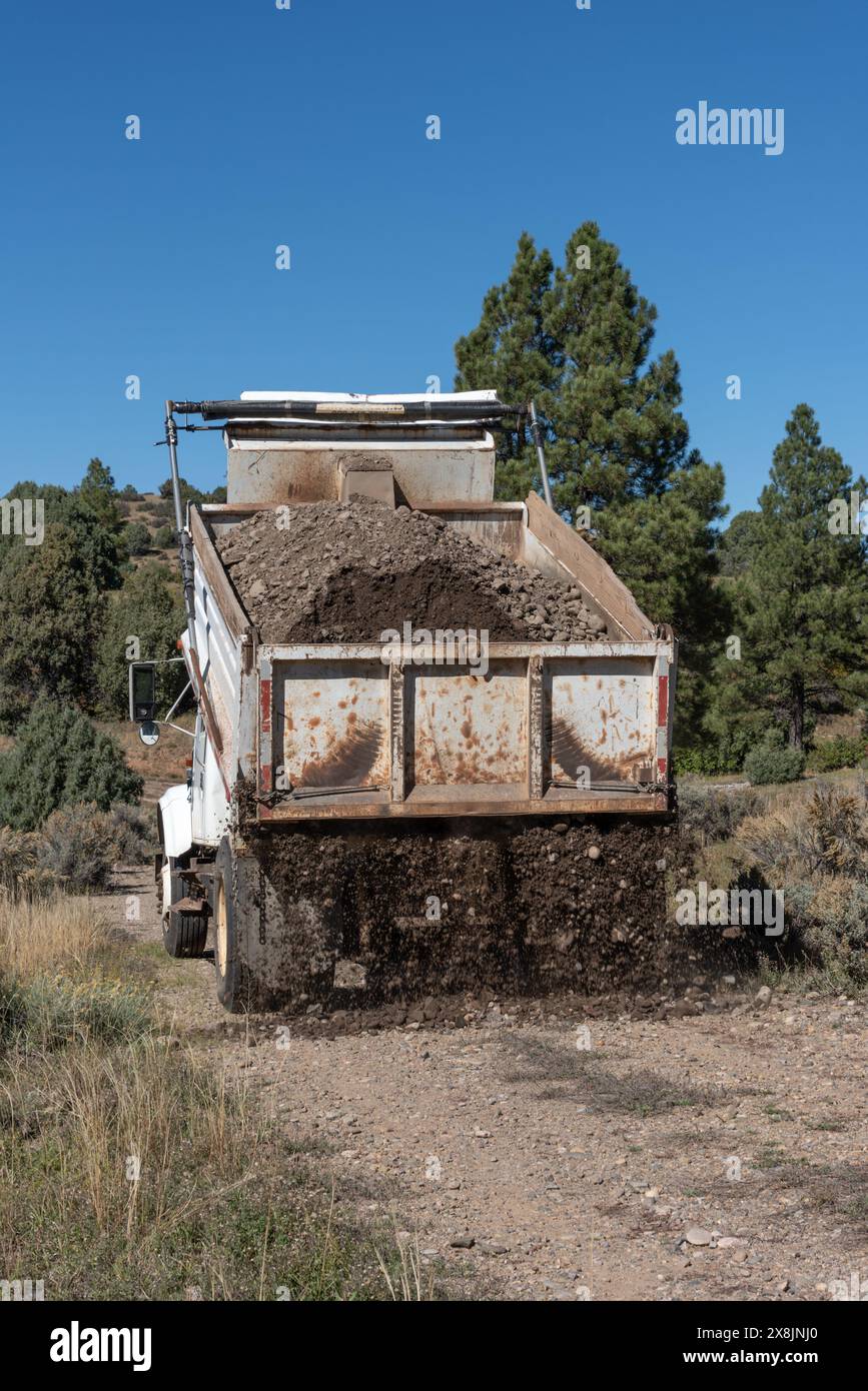 Old, white dump truck laying gravel on a road in a remote part of Northern New Mexico, USA. Stock Photo