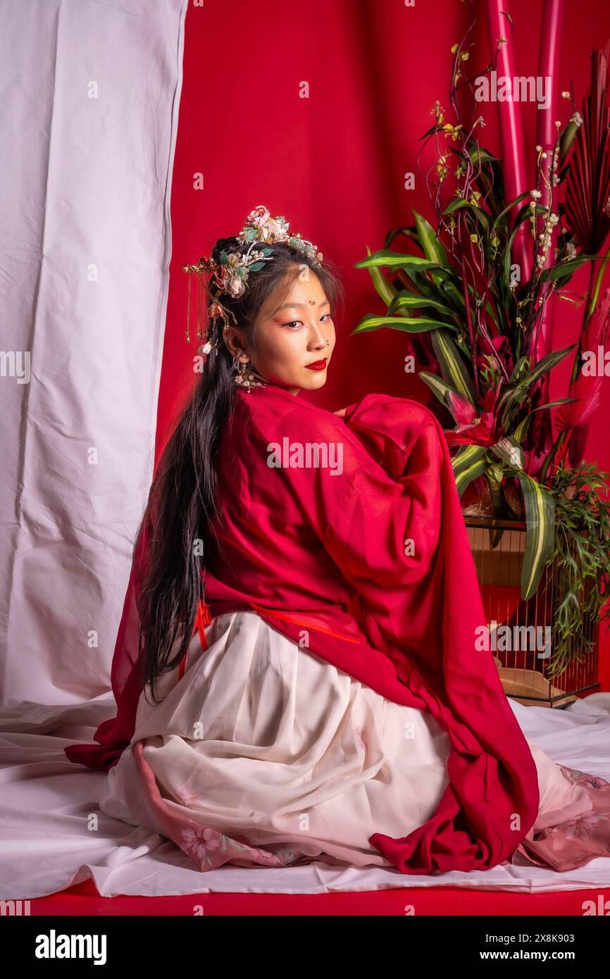 A woman in a red and white dress sits on a white surface. The woman is ...