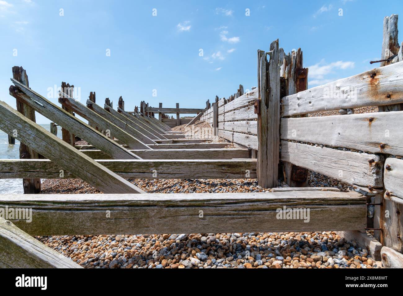 Old wooden sea defences and breakwaters at Rye Harbour with heavy diagonal and horizontal support beams, damaged and worn away by the sea. Stock Photo