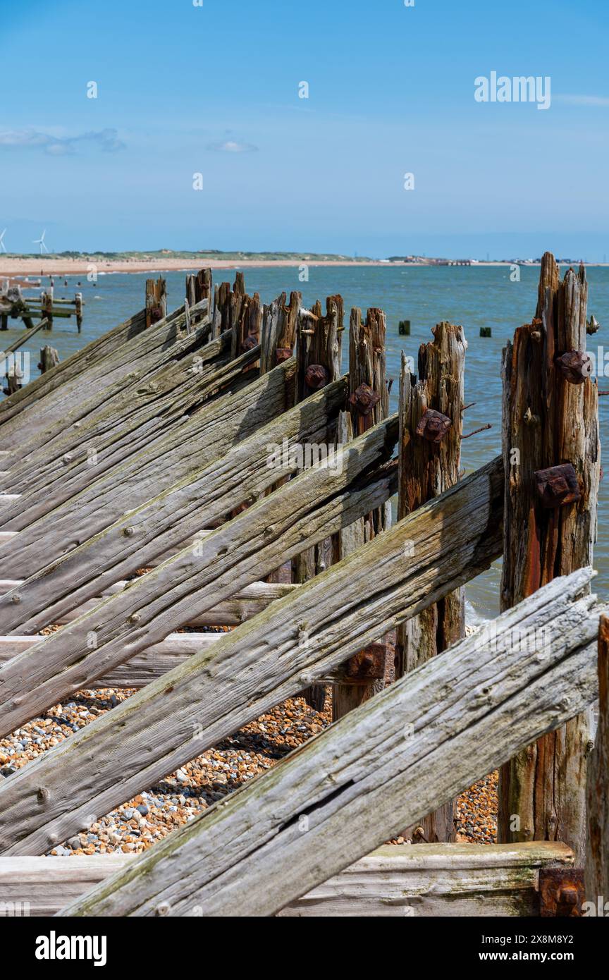 Old wooden sea defences and breakwaters at Rye Harbour with heavy diagonal and horizontal support beams, damaged and worn away by the sea. Stock Photo