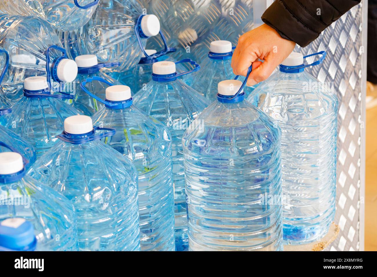 In the image, a hand is extending towards a bottle of water. The bottle appears to be blue and likely contains mineral drinking water, a clear fluid Stock Photo