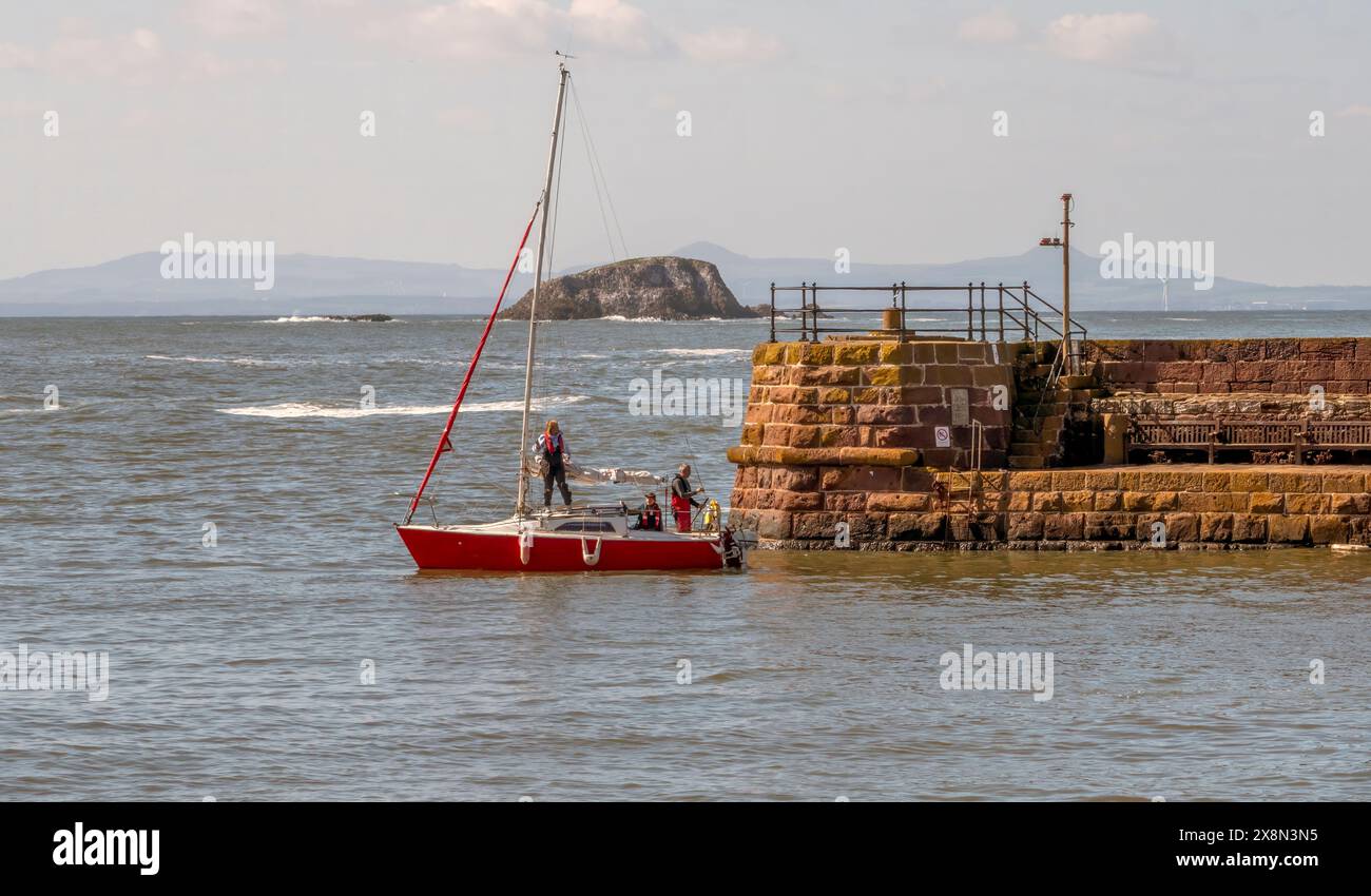 Small yacht leaving North Berwick harbour, East Lothian, UK - Lamb island, owned by Mr Uri Geller, in the distance. Stock Photo