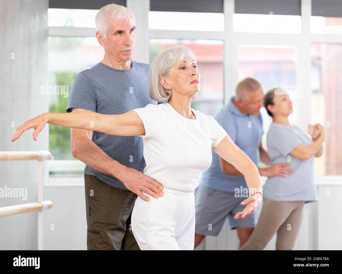 Elderly pairs dancers exercising various ballet moves during training with group of sporty people in training room Stock Photo
