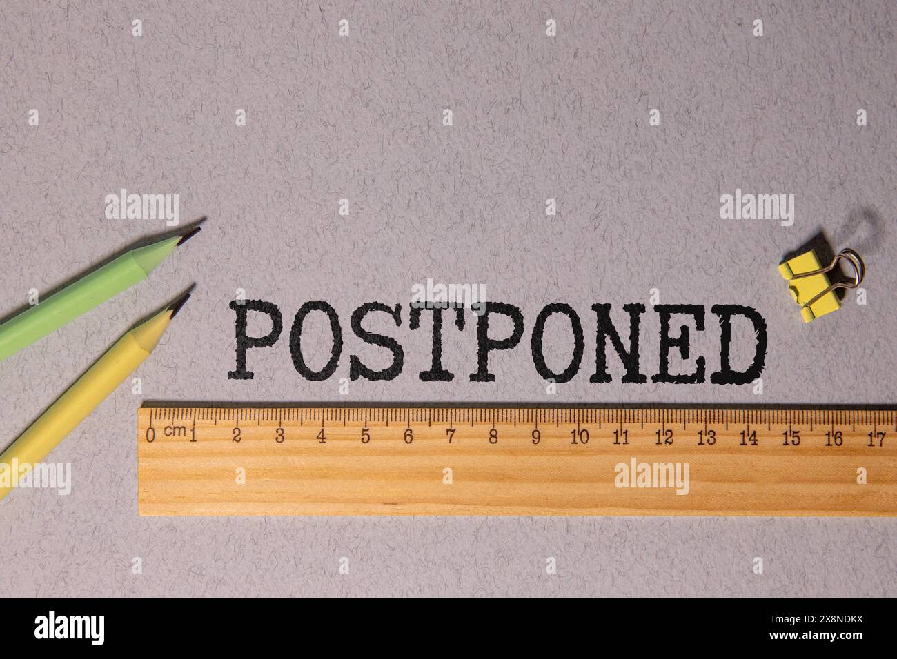 The word POSTPONED is written in a white notepad near a white cup of coffee on a light background. Stock Photo