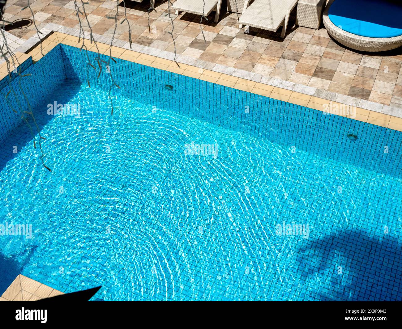 Top view space of blurred round rippled clear water moving on blue grid mosaic tiles in swimming pool background, near sunbed. Empty space on poolside Stock Photo