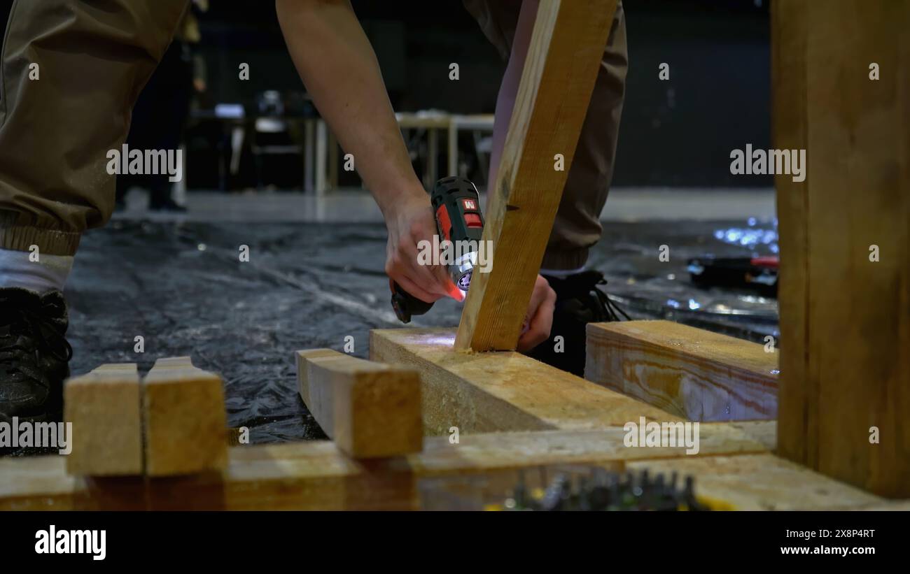 Carpenter working at workshop. Media. Worker using a screwdriver for assembling wooden construction. Stock Photo