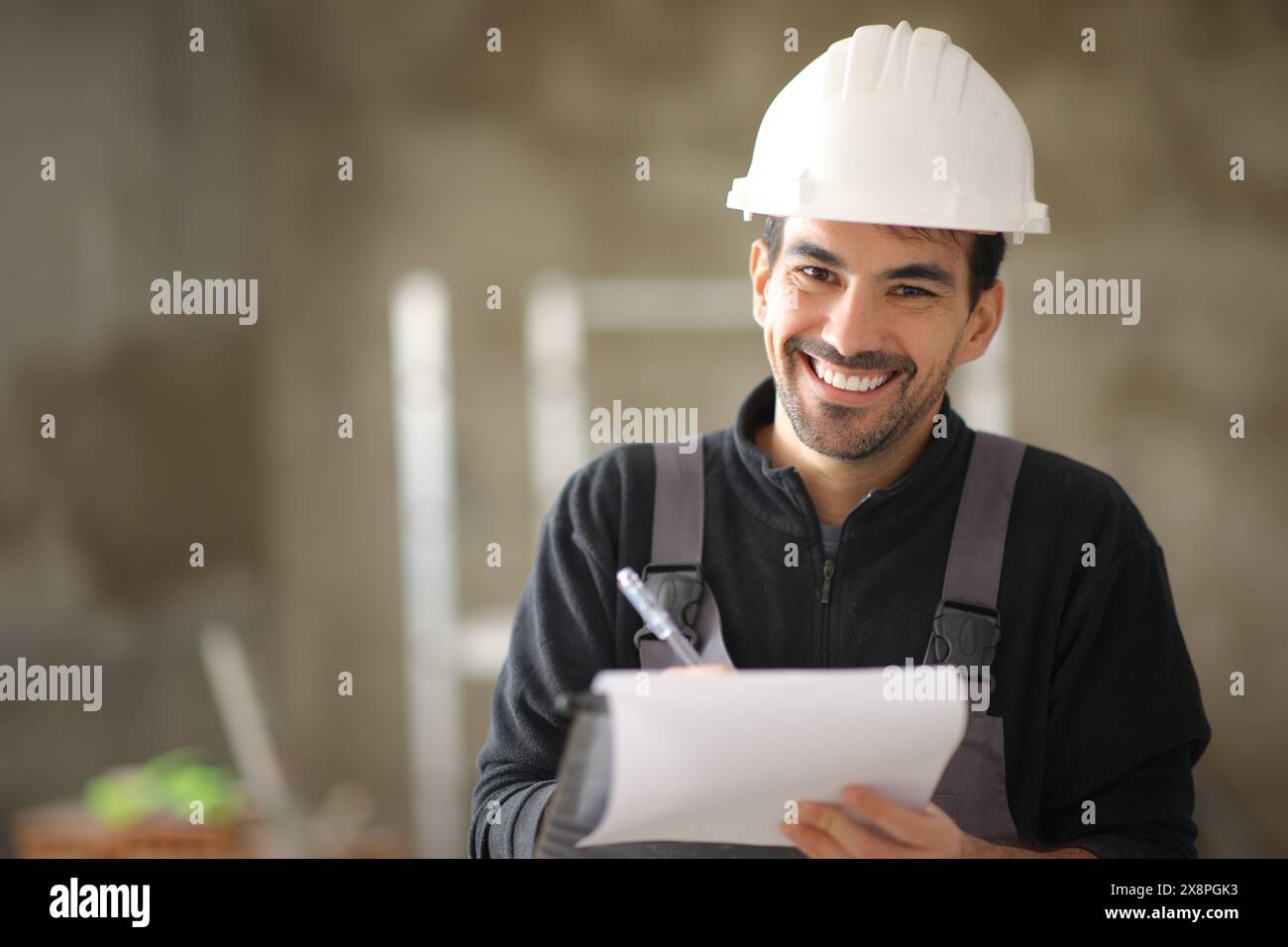 Happy construction worker holding clipboard looking at you in a house Stock Photo