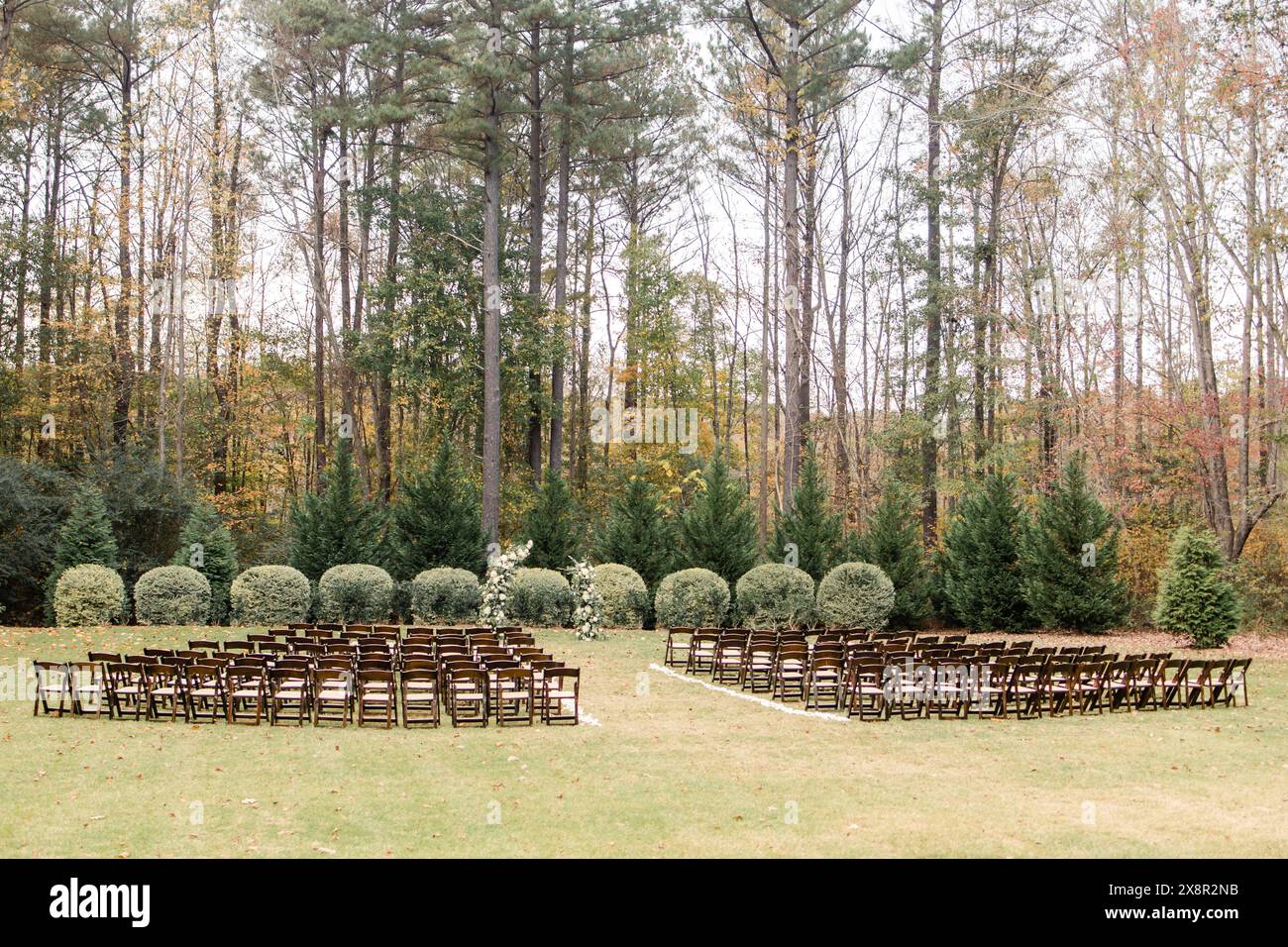 Outdoor wedding ceremony with rows of wooden chairs by trees Stock Photo