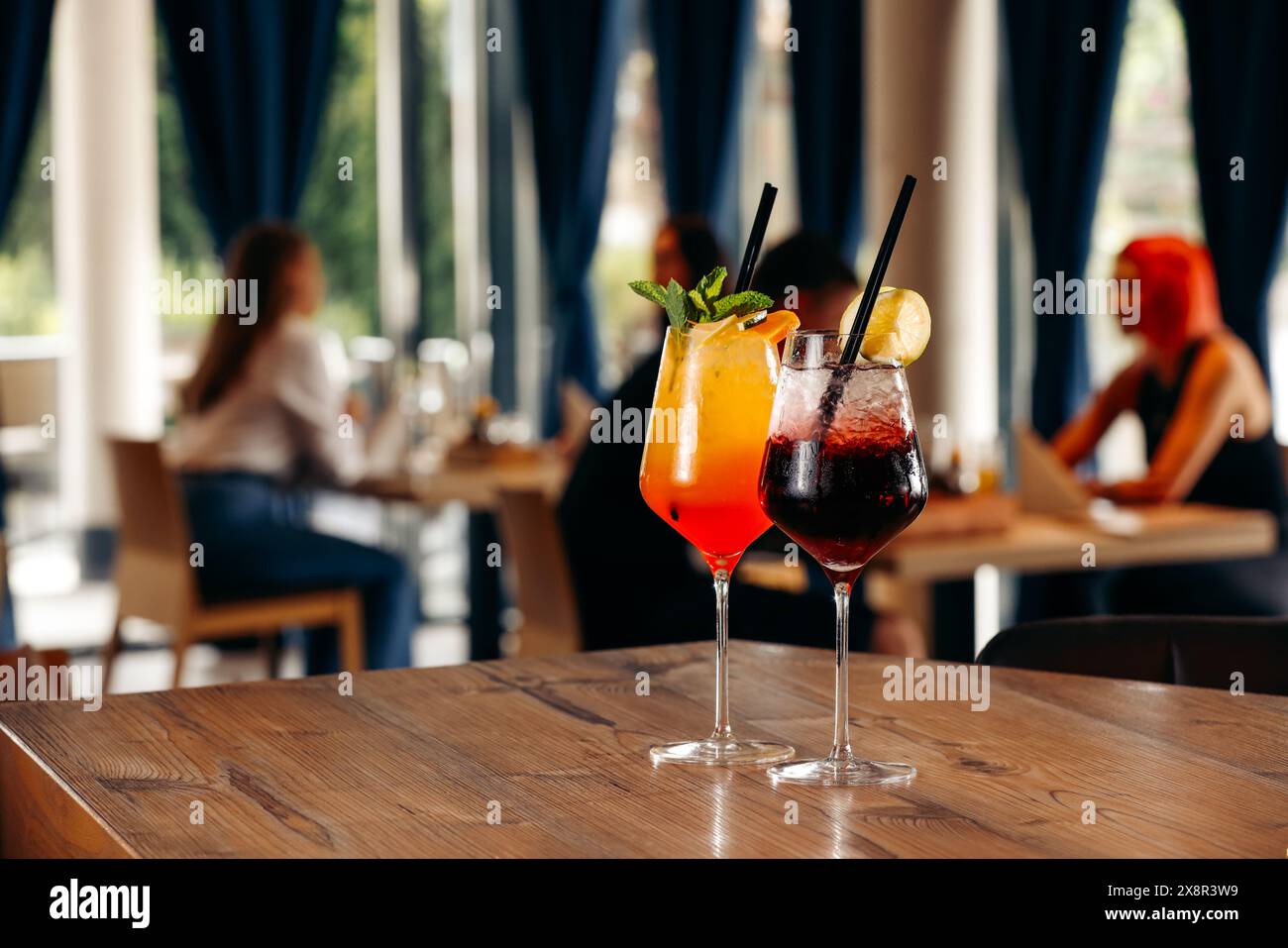 Two colorful cocktails on a restaurant table with people Stock Photo