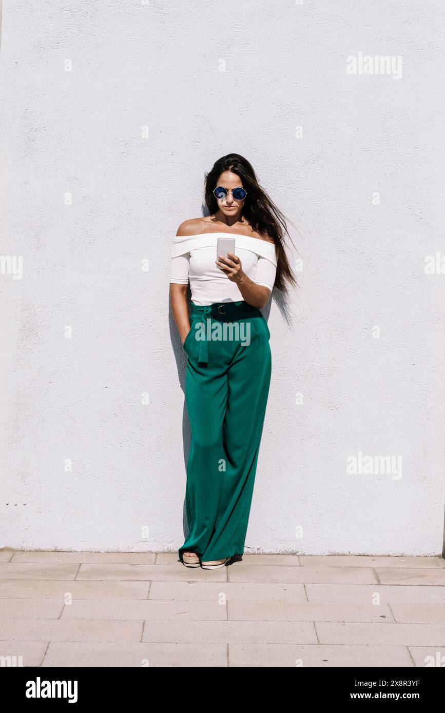 Beautiful woman in sunglasses leaning while using a mobile phone Stock Photo