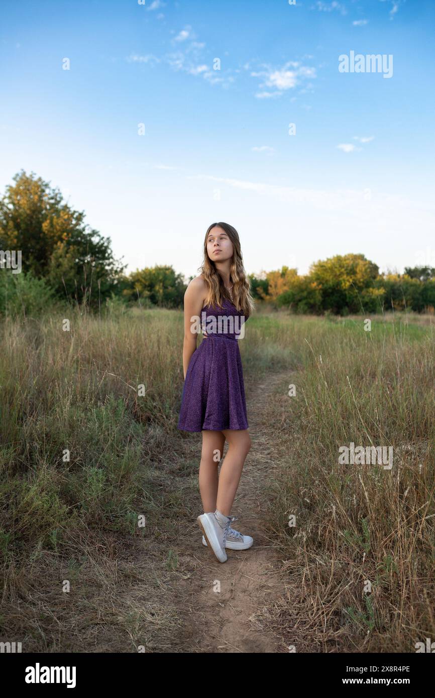 sixteen-year-old-girl-in-a-purple-dress-standing-in-a-field-stock-photo
