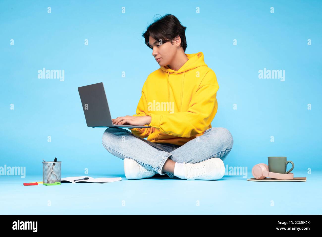 Young Guy Working on Laptop in Studio With Blue Background Stock Photo