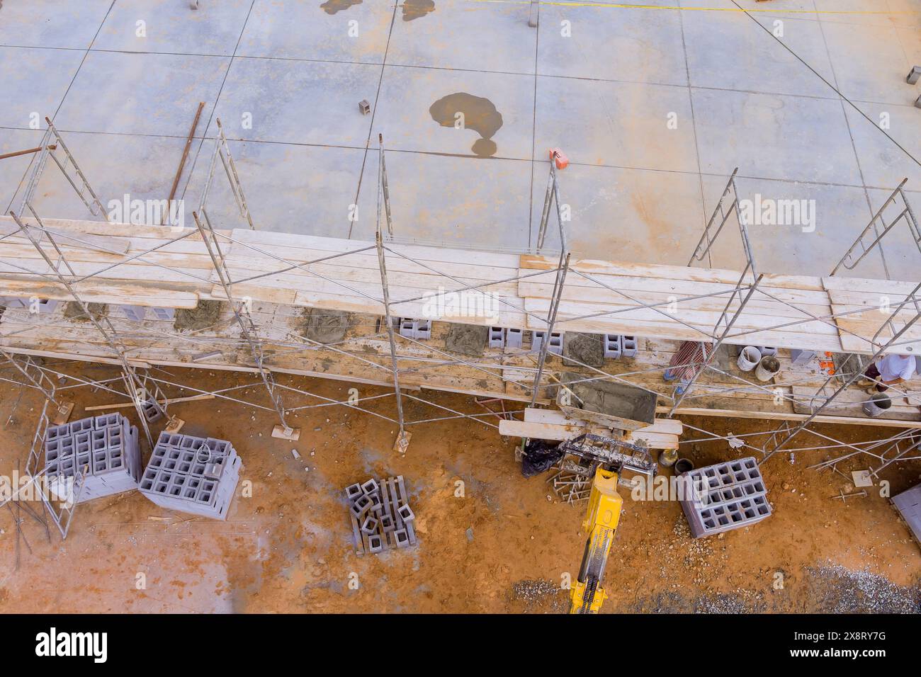 Masonry worker stands on scaffolding while making concrete wall using cement blocks Stock Photo