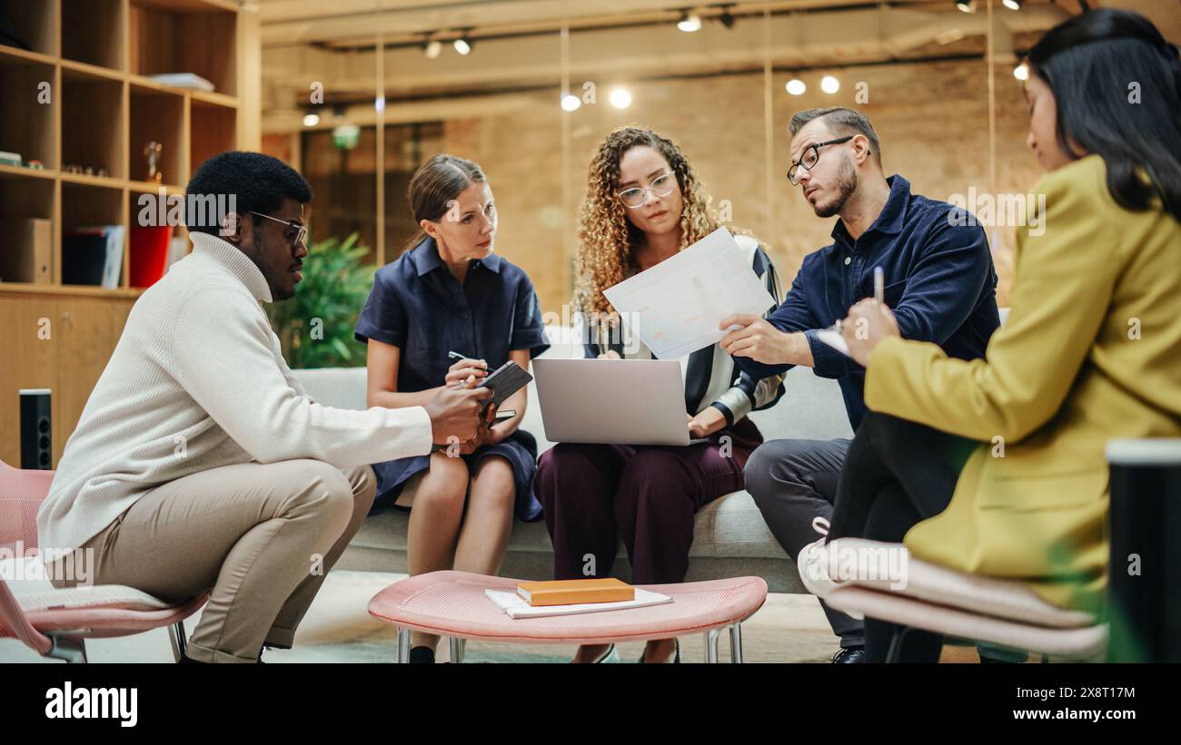 Multi Ethnic Group of People Working on Developing Growth Ideas Based on Data. Energetic Teammates in a Meeting Room in an Office, Analyzing Charts Using Tablet and Laptop. Wide Shot Stock Photo