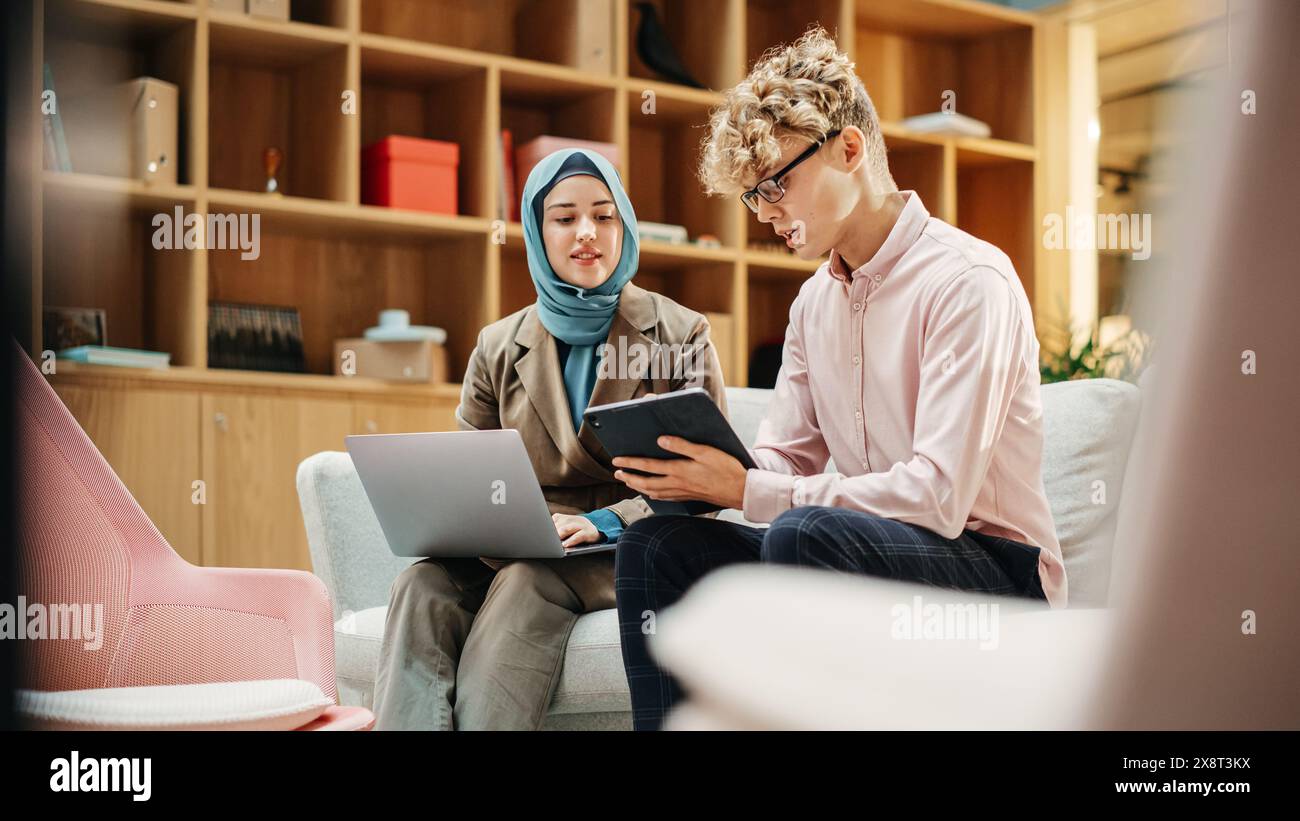 Two Creative Colleagues Collaborating Over a Work Project Using Computer and Tablet at Office. Male E-commerce Marketing Manager Discussing with Muslim Female Media Planner. Medium Stock Photo