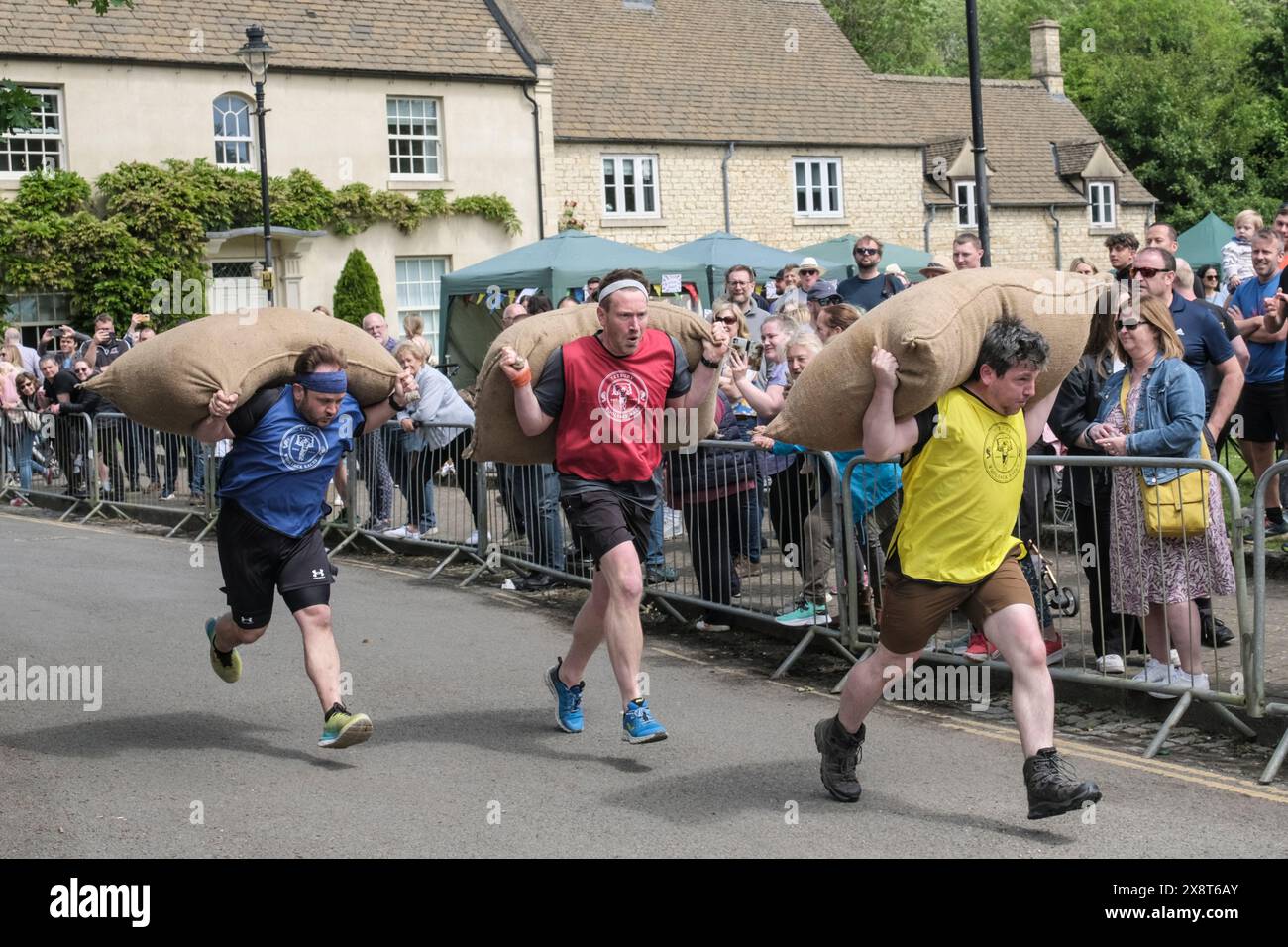 Tetbury, Gloucestershire, UK. 27th May, 2024. Woolsack races return to Tetbury after a 5-year hiatus. Competitors race up the steep 1 in 4 gradient of Gumstool Hill in this pretty Cotswold town carrying a woolsack. The men carry a 60lb sack and the ladies a 30lb sack. The annual races attract large crowds and raise money for local charities. Credit: JMF News/Alamy Live News Stock Photo