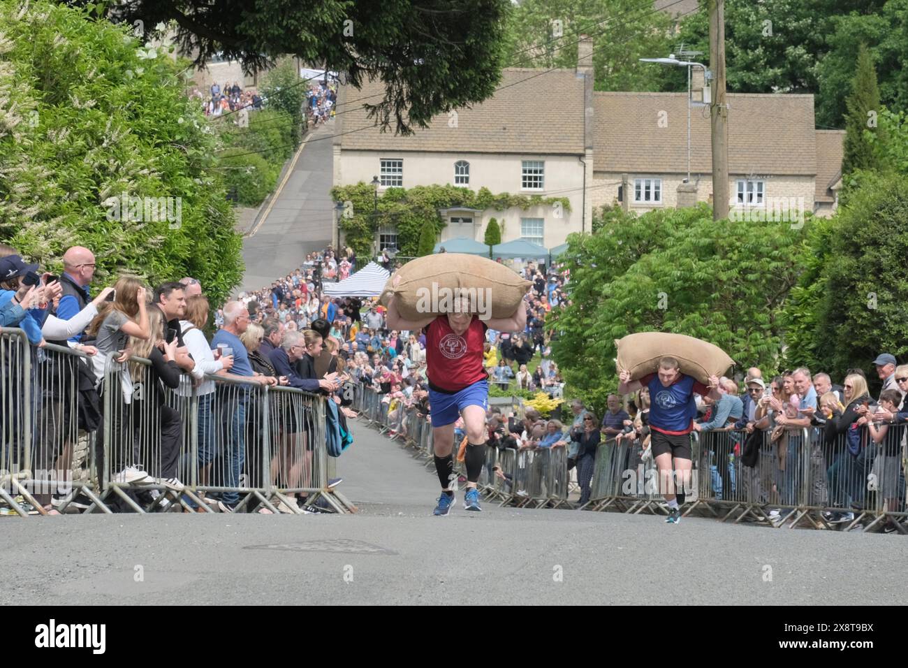 Tetbury, Gloucestershire, UK. 27th May, 2024. Woolsack races return to Tetbury after a 5-year hiatus. Competitors race up the steep 1 in 4 gradient of Gumstool Hill in this pretty Cotswold town carrying a woolsack. The men carry a 60lb sack and the ladies a 30lb sack. The annual races attract large crowds and raise money for local charities. Credit: JMF News/Alamy Live News Stock Photo