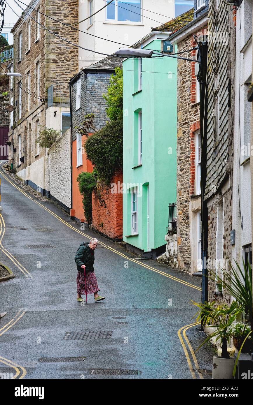 A lone figure walking down the steep Tregoney Hill with colourful old cottages in Mevagissey Cornwall England UK Stock Photo