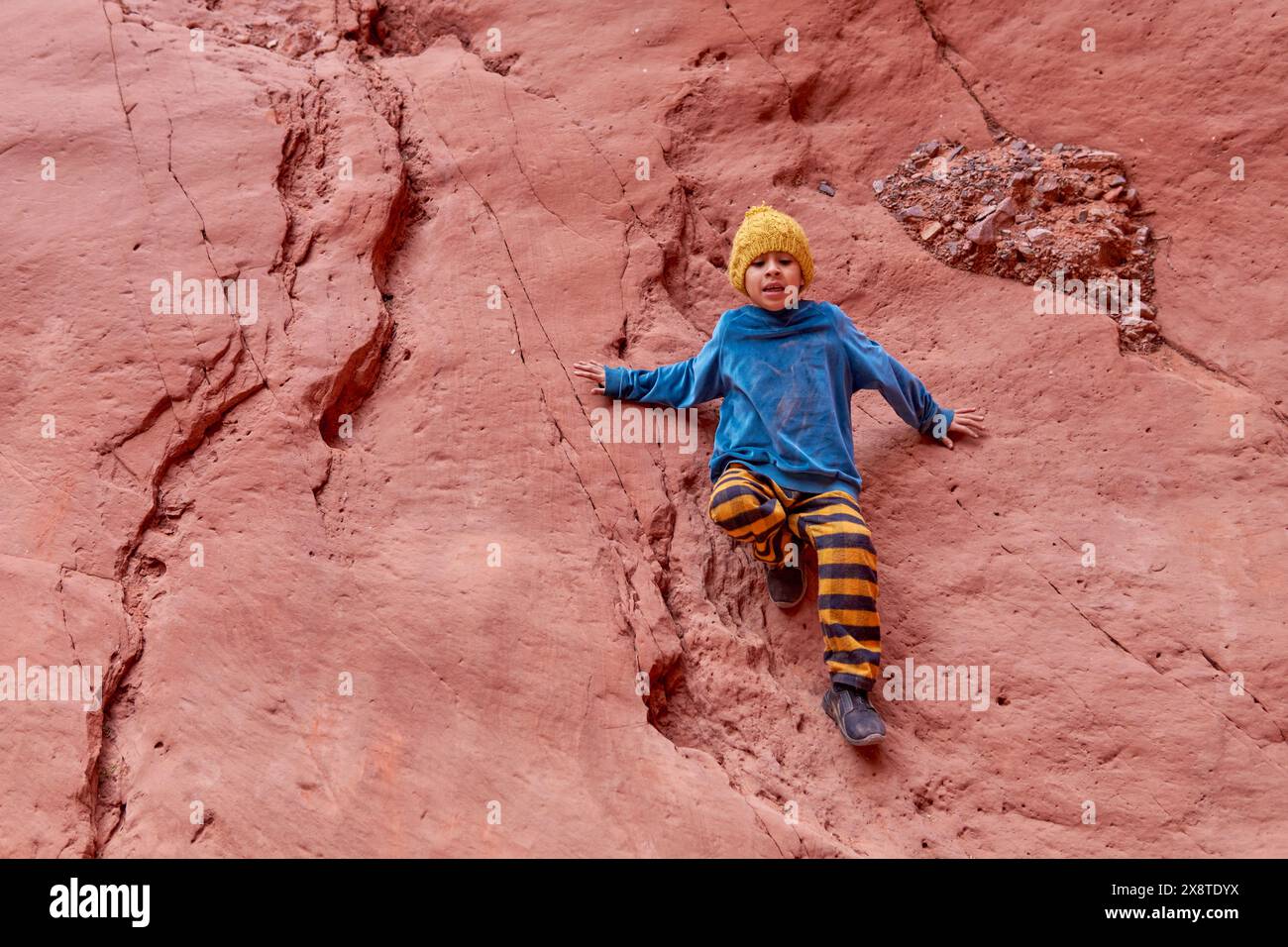 latin boy sitting falling scared from a rock formation on an excursion in the quebrada de las señoritas in Jujuy, Argentina. Stock Photo