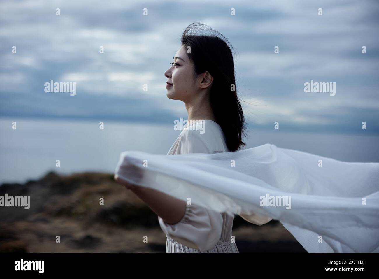 Japanese woman in white dress standing on a hill overlooking the ocean ...