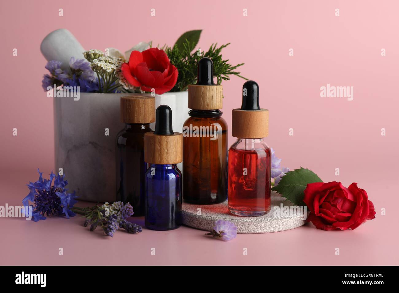 Aromatherapy. Different essential oils, flowers, mortar and pestle on pink background Stock Photo