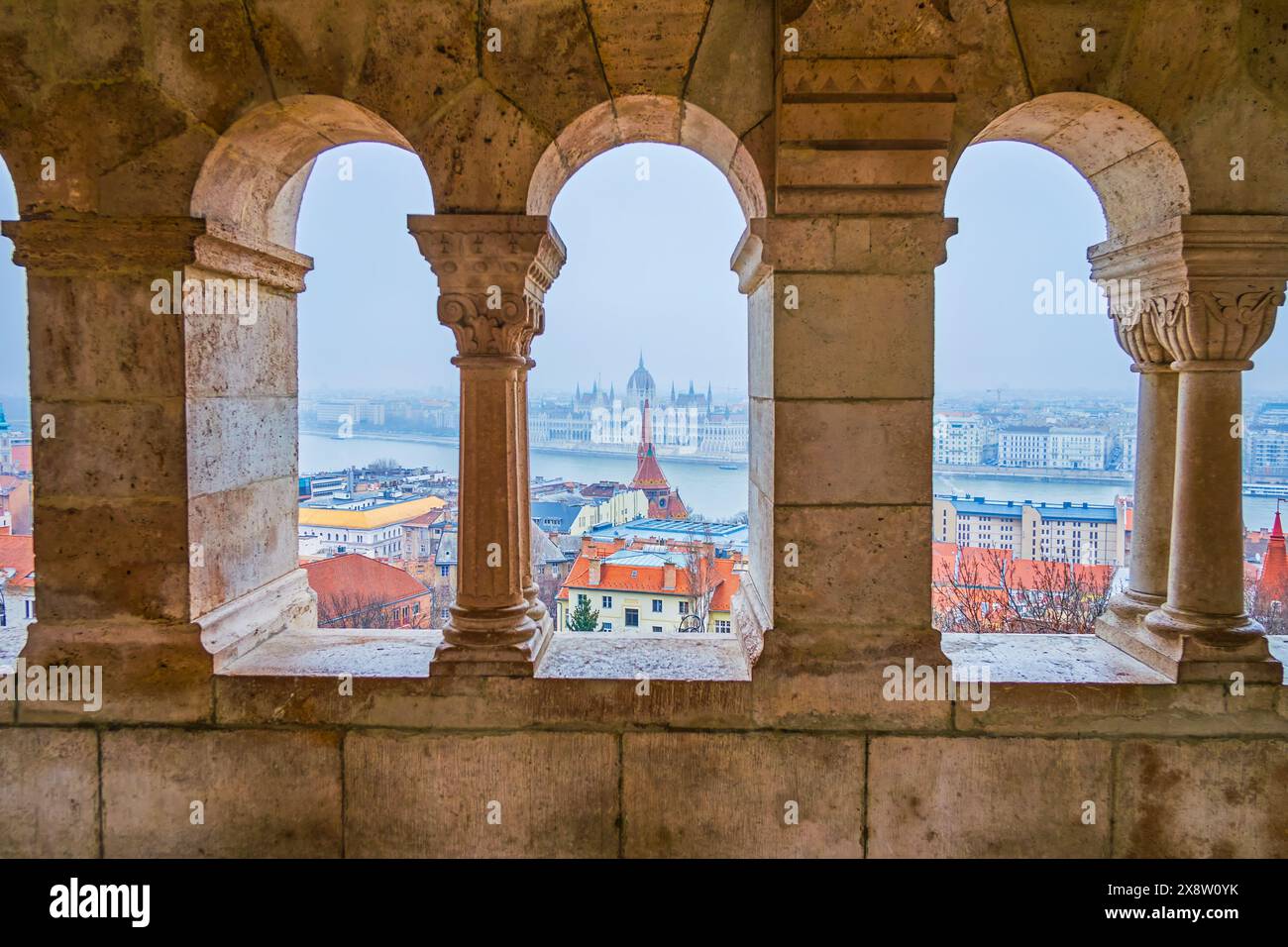 The view through the windows of the arcade at Fisherman's Bastion, showcasing Parliament, houses and the Danube River in Budapest, Hungary. Stock Photo