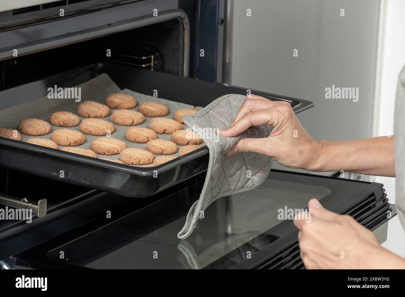 person's hands using an oven mitt to remove a tray of cookies from an oven Stock Photo