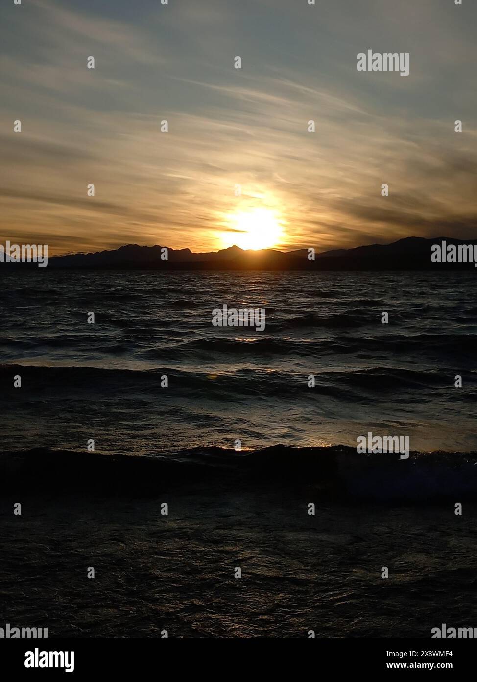 Golden sunset casting warm hues over a serene lake with gentle waves ...
