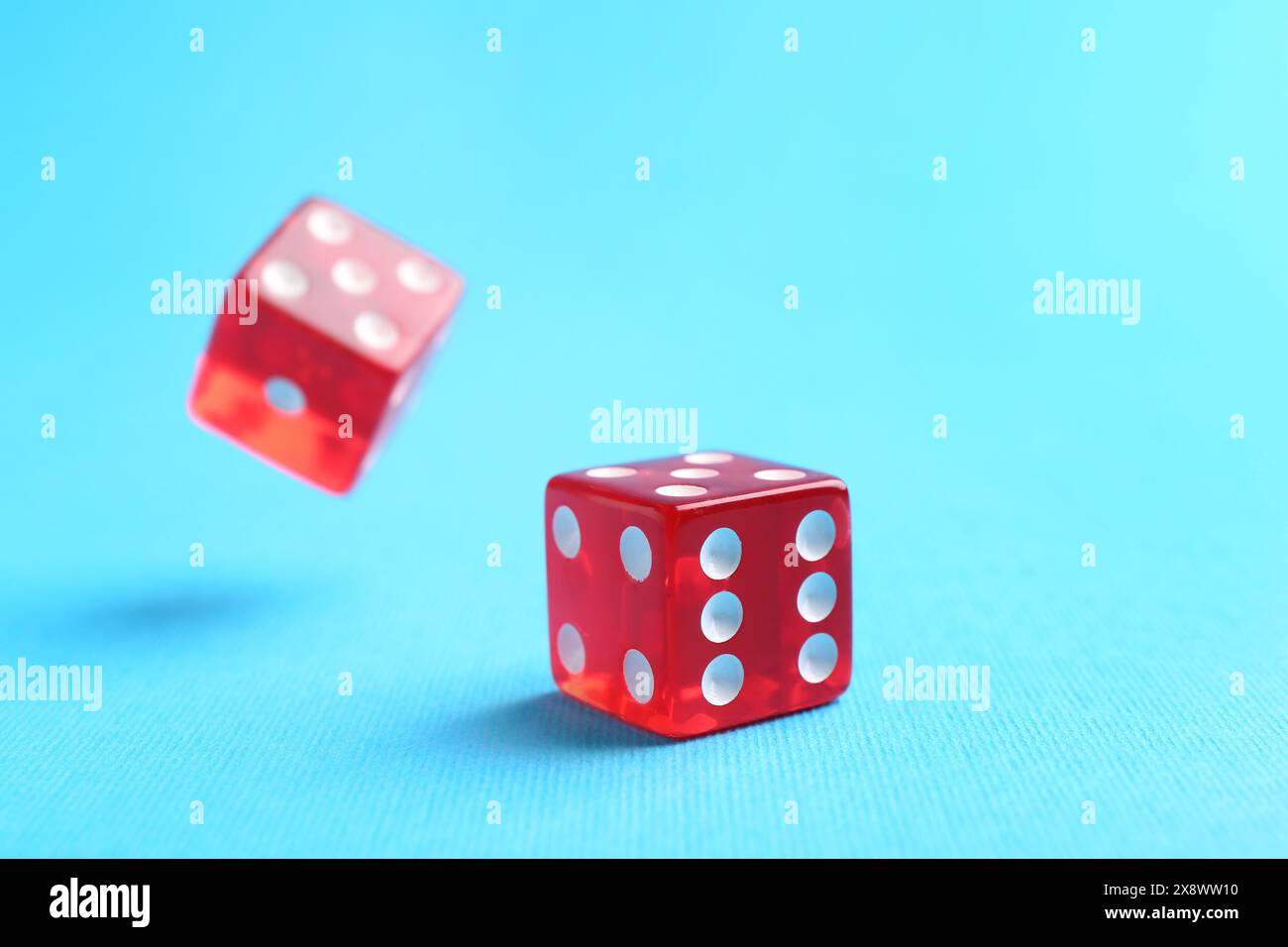 Two red game dices falling on light blue background, closeup Stock Photo