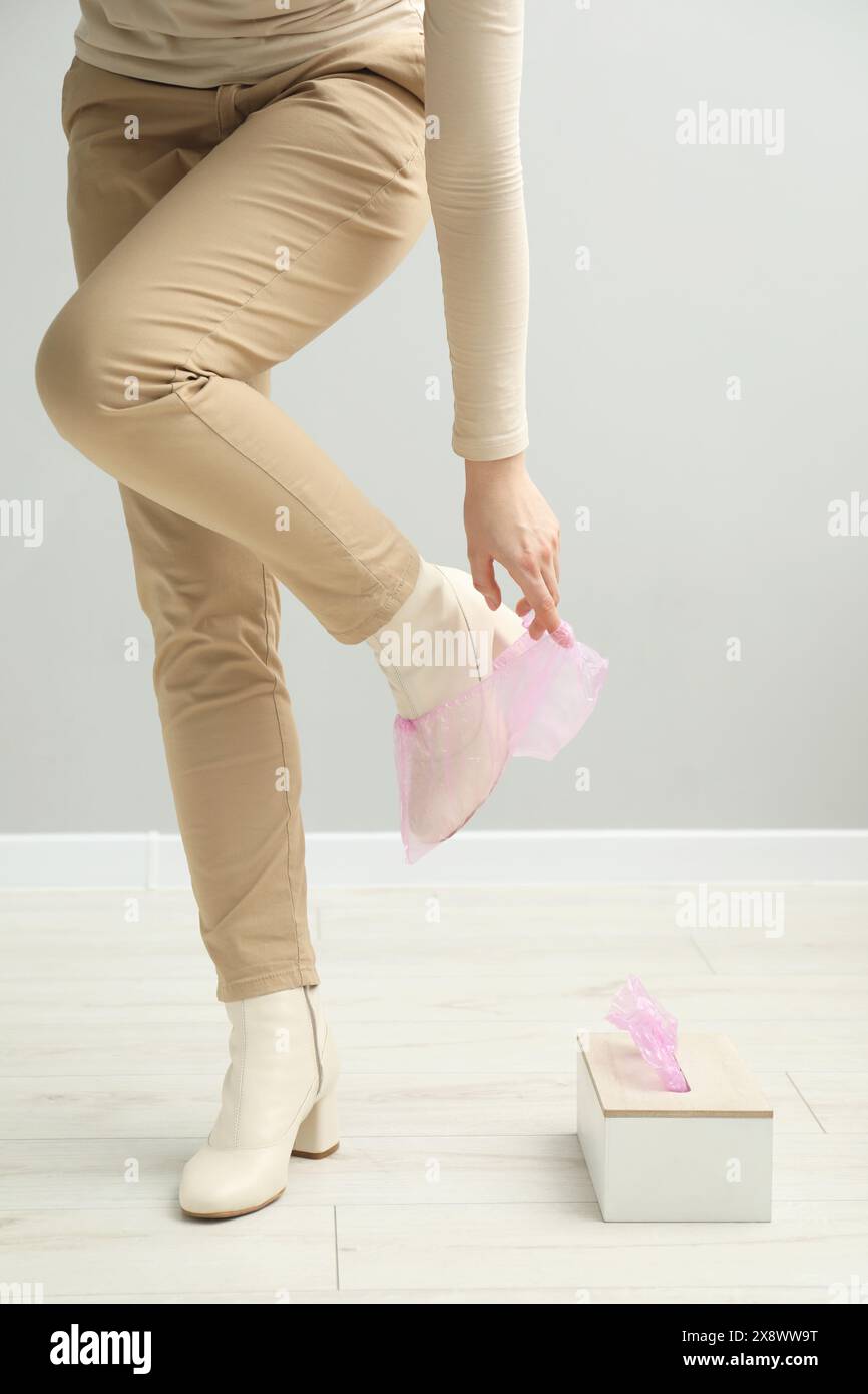 Woman wearing pink shoe cover onto her boot indoors, closeup Stock Photo