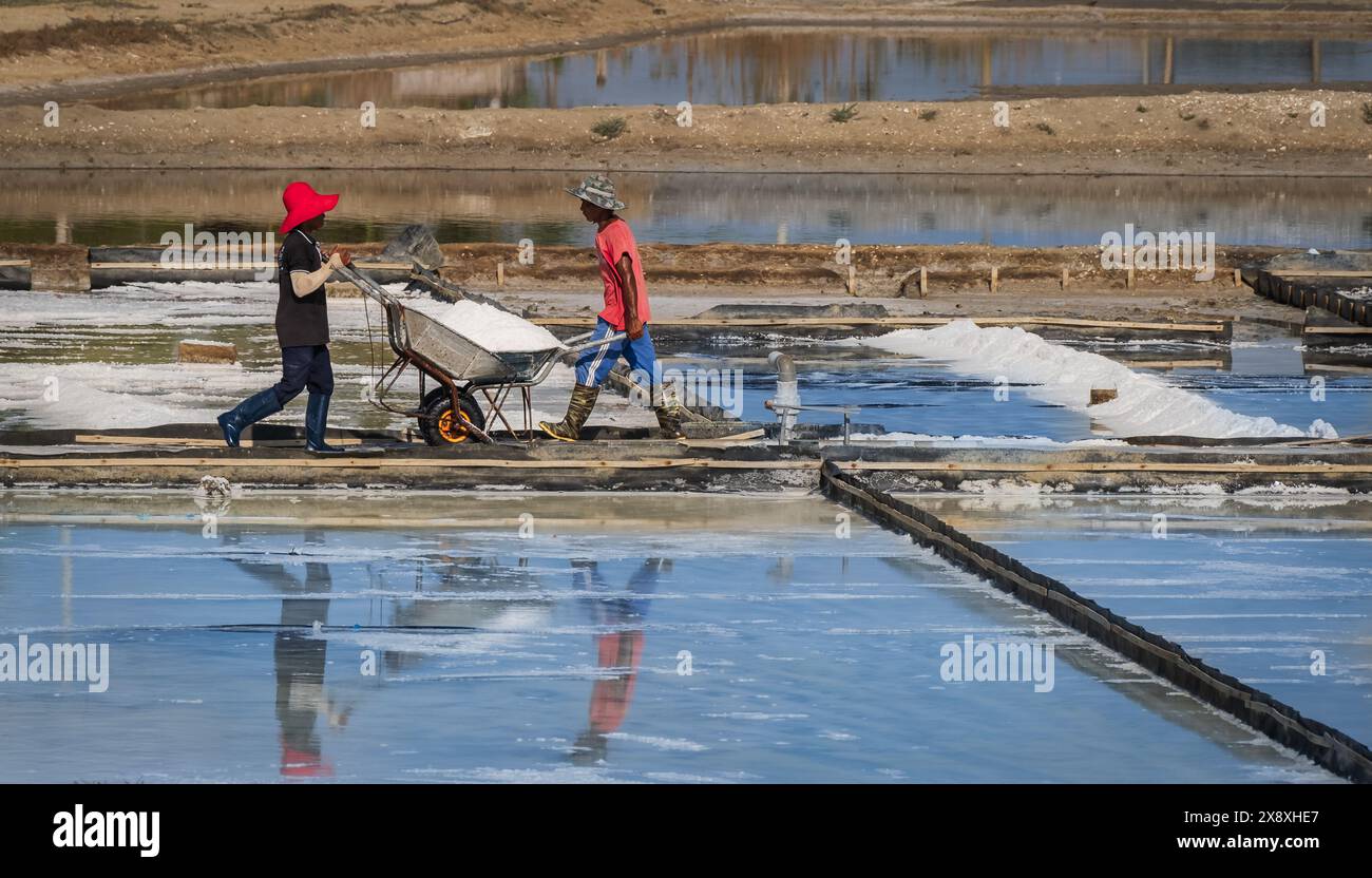 A salt farmers is harvesting salt under the hot summer sun. villagers working on salt farms in Vietnam. Hard working men. Two men caring salt in the t Stock Photo