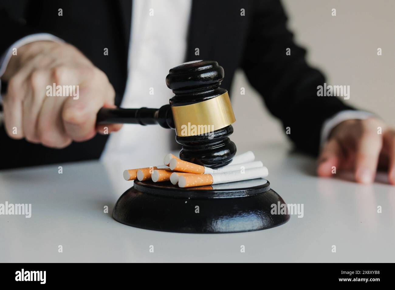Judge hitting cigarettes with referee's gavel on white table. Tobacco
