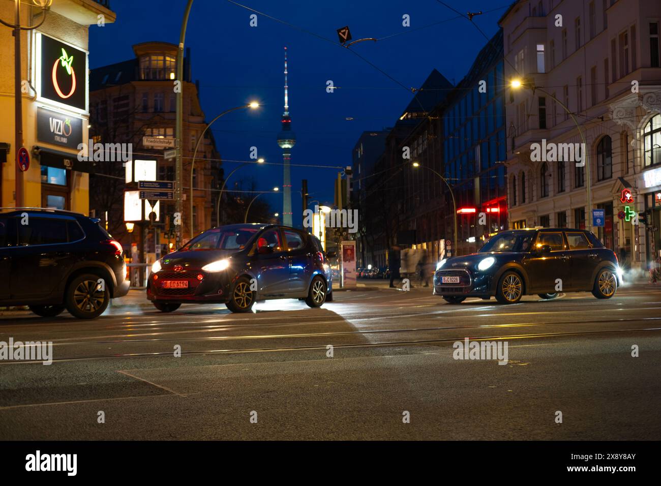 Cars driving down night Oranienburger street, Illuminated buildings and Fernsehturm TV tower visible in background, Nightlife, sustainability and envi Stock Photo