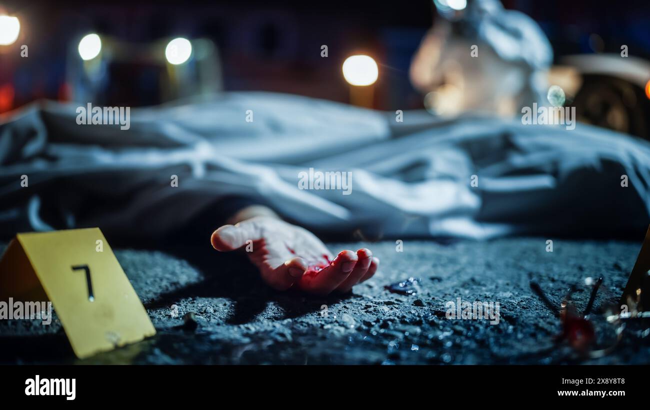 Bloody Hand of a Dead Body Peeking out of Cloth Cover at a Crime Scene. Forensics Team Taking Photos of the Victim's Corpse for Documentation and Investigating. Evidence and Clues are Scattered Around Stock Photo