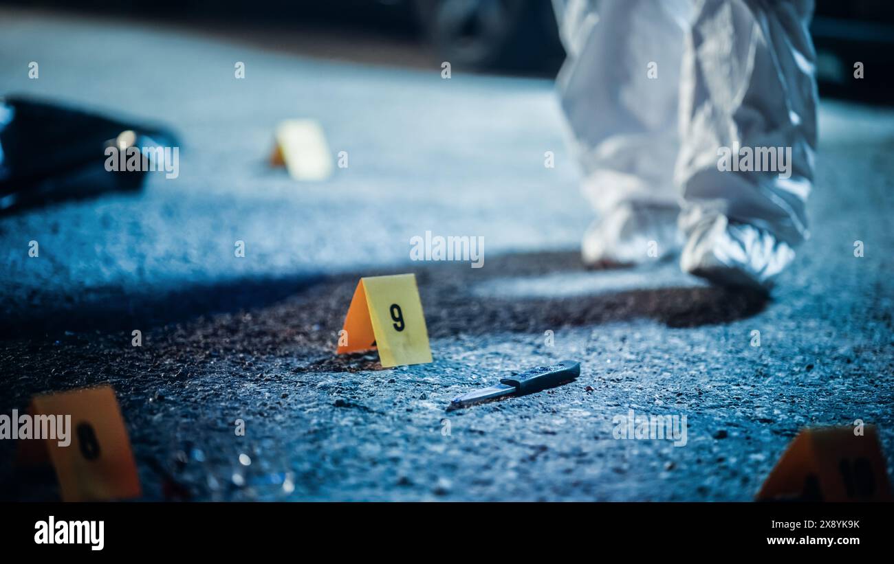 Expert in Coveralls Starting to Pack Evidence on Crime Scene After a Tragic Ending of a Violent Street Fight. Bloody Knife Identified as the Murder Weapon Used to Stab the Victim is Found on Spot Stock Photo