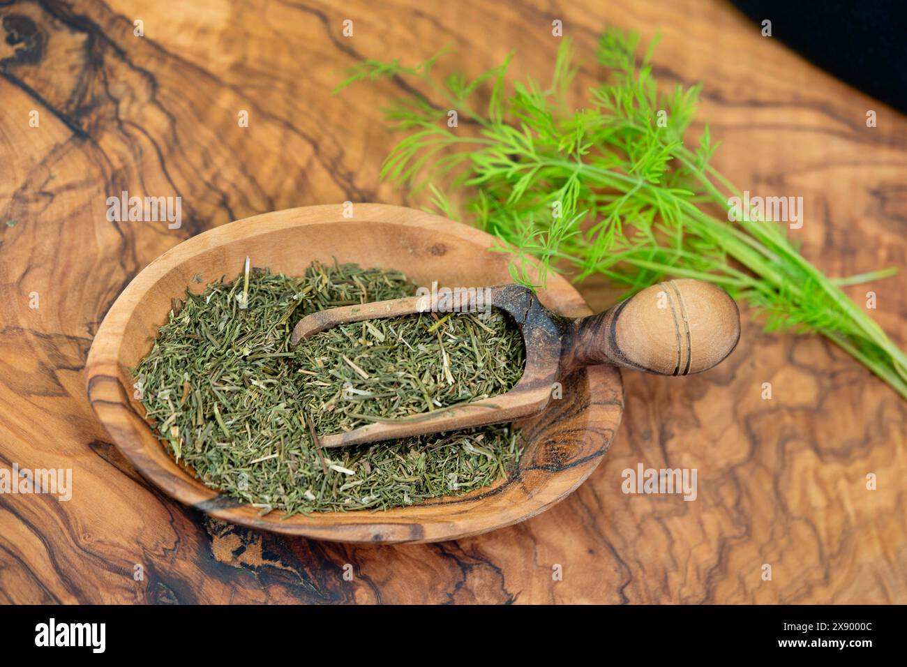 dill (Anethum graveolens var. hortorum), dried and chopped herb in a wooden bowl and on wooden shovels Stock Photo