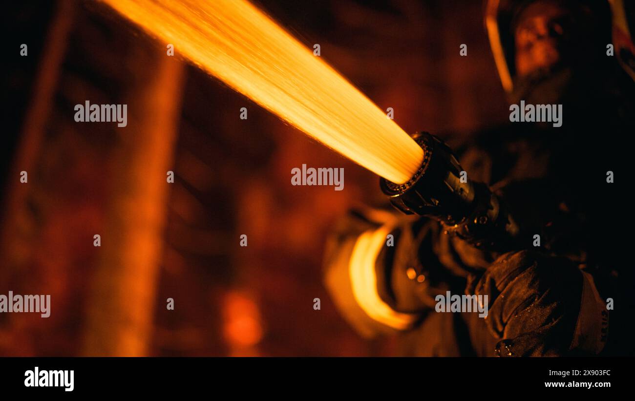 Close Up Low Angle Creative Portrait of a Brave African American Firefighter Using a Firehose to Fight a Forest Fire. Focus on Black Fireman Hands Holding High-Pressure Water Hose. Stock Photo