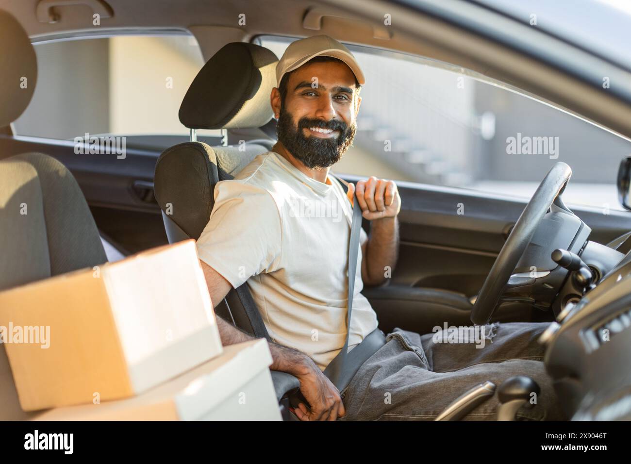 Driver Smiling While Fastening Seatbelt in Car With Packages Stock Photo