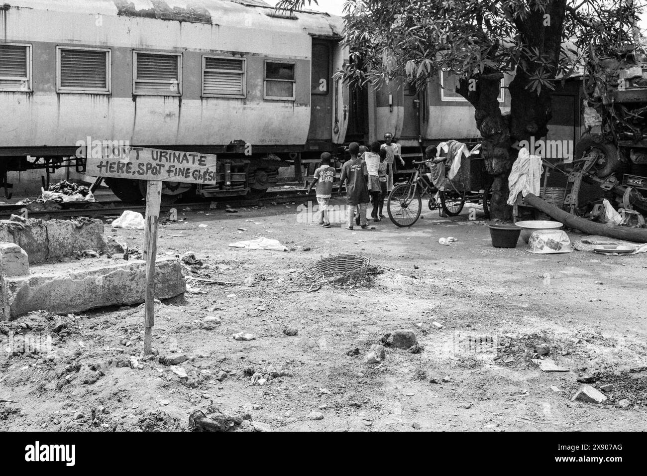 Group of children playing near an old train carriage with a 'Don't Urinate Here, Spot Fine GHS50' sign in a market area in Accra, Ghana Stock Photo