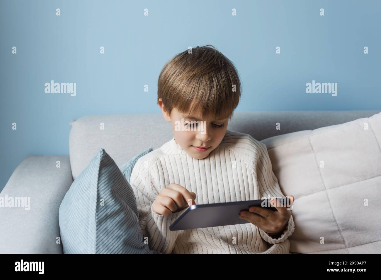 Boy is relaxing on the sofa at home and using a tablet. Stock Photo