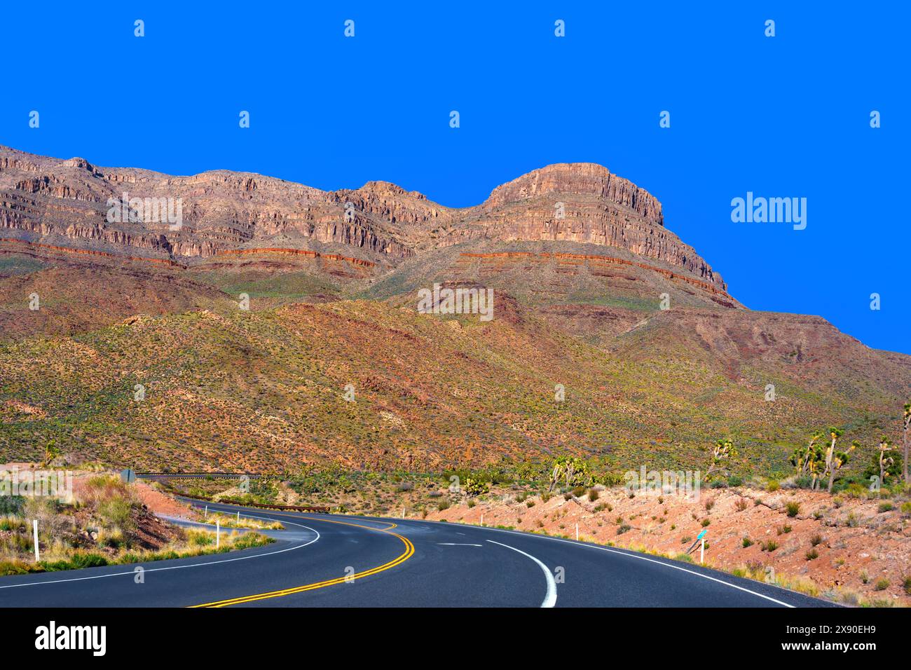 Asphalt road with bright yellow dividing lines winds through Arizona's rugged terrain under the clear blue sky. Stock Photo