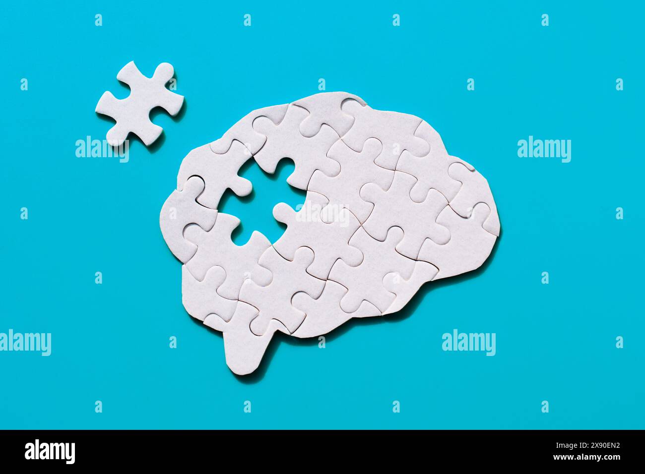 Incomplete jigsaw puzzle in the shape of a brain on a blue background. Acquiring knowledge and forming mind connections. Stock Photo